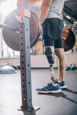 cropped shot of man with artificial leg working out with barbell at gym clipart