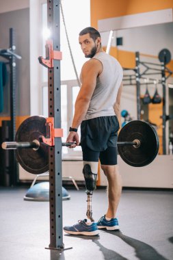 athletic sportsman with artificial leg working out with barbell at gym clipart