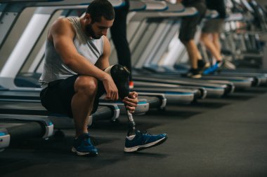 yakışıklı genç sporcu spor salonunda koşu bandı üzerinde oturan yapay bacak ile
