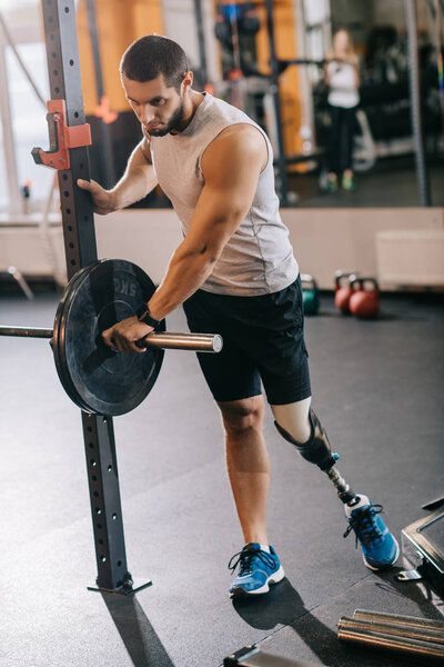 athletic young sportsman with artificial leg preparing for workout with barbell at gym