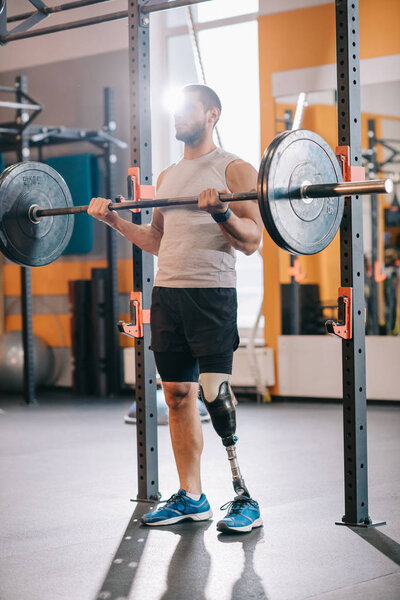 muscular young sportsman with artificial leg working out with barbell at gym