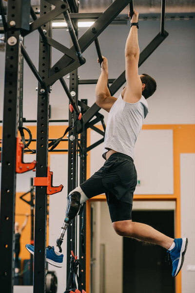 атлетичный молодой спортсмен с искусственной ногой работает с гимнастической лестницей в тренажерном зале
