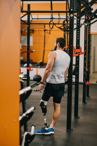 athletic young sportsman with artificial leg standing near gymnastics ladder at gym