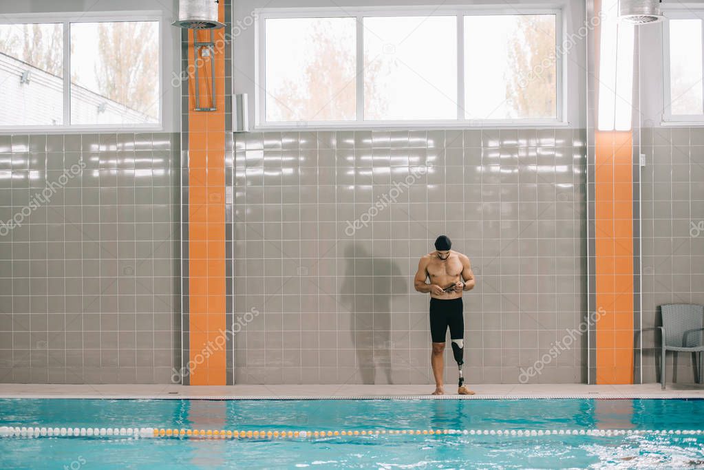 handsome young sportsman with artificial leg standing on poolside at indoor swimming pool