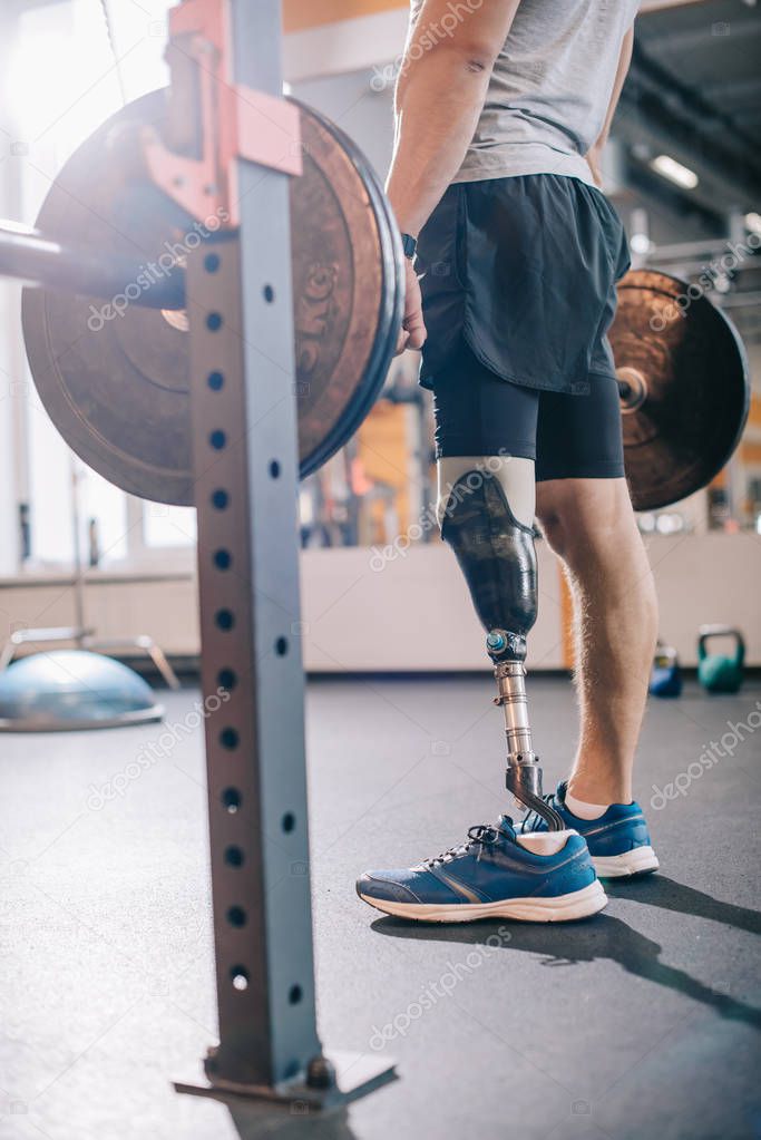 cropped shot of man with artificial leg working out with barbell at gym