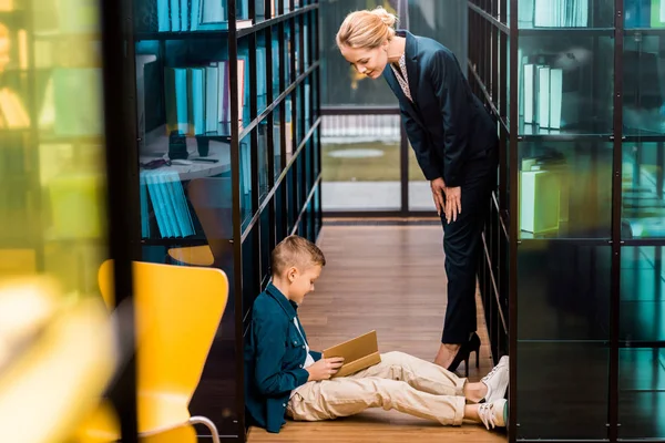 Side View Young Female Librarian Looking Boy Reading Book Floor — Stock Photo, Image