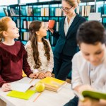 Lachende jonge vrouwelijke leraar kop te houden en te kijken naar schoolkinderen in bibliotheek