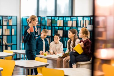 Genç kadın kütüphaneci ve birlikte kitaplıkta konuşurken schoolkids