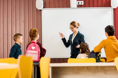 Genç öğretmen okul çocukları ile sırt çantaları sunuya yapma gülümseyen