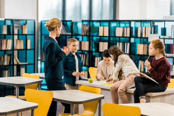 Młoda Kobieta Bibliotekarz Trzyma Puchar Ogląda Schoolkids Czytanie Książek Bibliotece — Zdjęcie stockowe