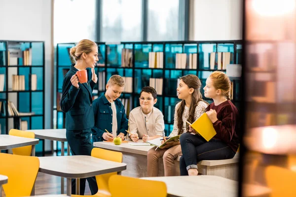 Fiatal Női Könyvtáros Schoolkids Beszélgettek Könyvtár — Stock Fotó