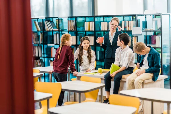 Young Female Librarian Holding Cup Looking Smiling Schoolchildren Library — Stock Photo, Image