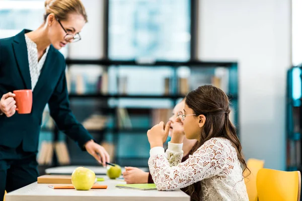 Young Teacher Holding Cup Looking Schoolgirls Studying Library — Free Stock Photo