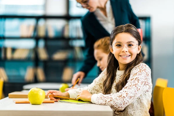 Aranyos Schoolkid Szemüvegek Mosolyogva Kamera Miközben Tanul Osztálytársa Tanár — Stock Fotó