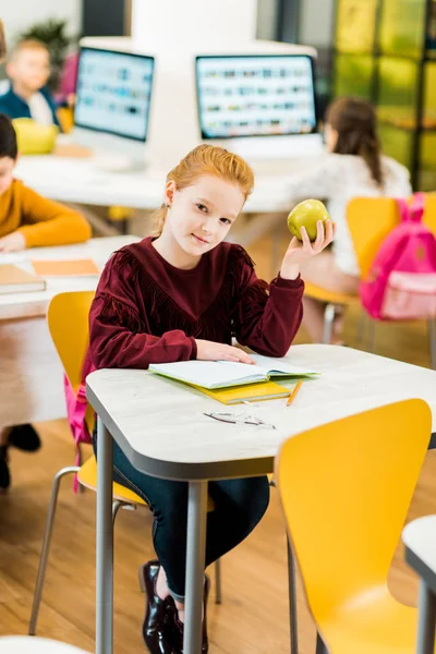 愛らしい Schoolkid Apple キーを押しながらライブラリで同級生と一緒に座ってカメラ目線  — 無料ストックフォト