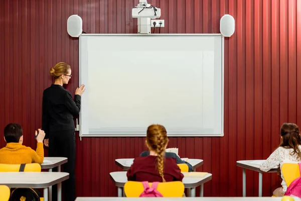 Vue Arrière Des Écoliers Assis Aux Bureaux Enseignant Faisant Présentation — Photo