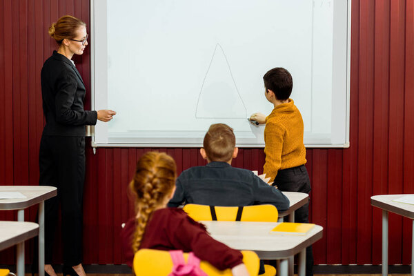 back view of schoolkids and teacher studying with interactive whiteboard behind  