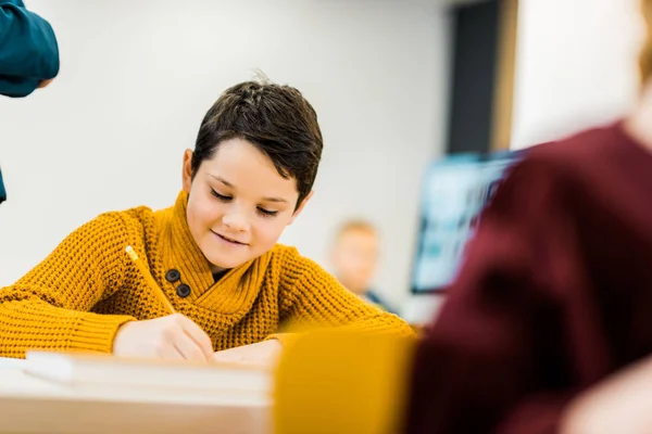 Netter Lächelnder Schuljunge Der Mit Bleistift Klassenzimmer Schreibt Stockfoto