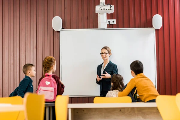 Jeune Enseignant Debout Près Tableau Blanc Interactif Regardant Les Écoliers Image En Vente