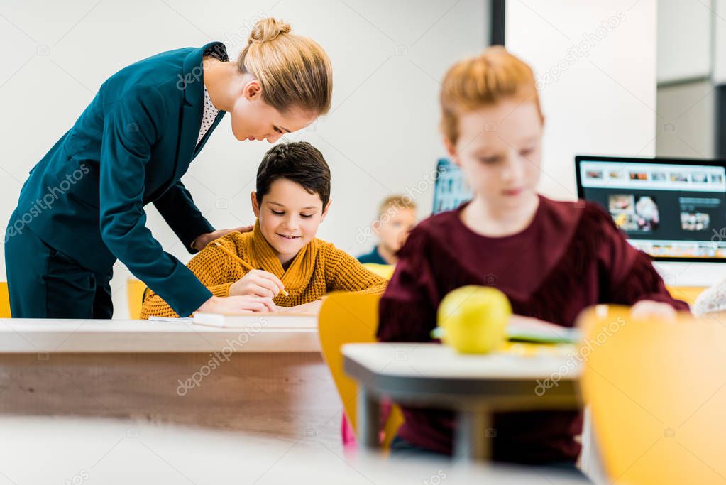 young teacher helping schoolchildren studying at desks 