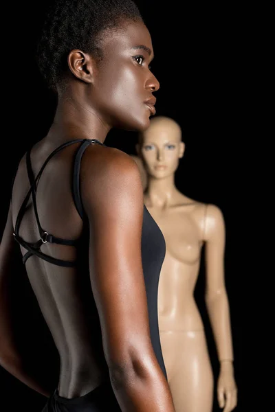 Vue latérale de la fille afro-américaine en maillot de bain regardant loin tout en se tenant près du mannequin sur noir — Photo de stock