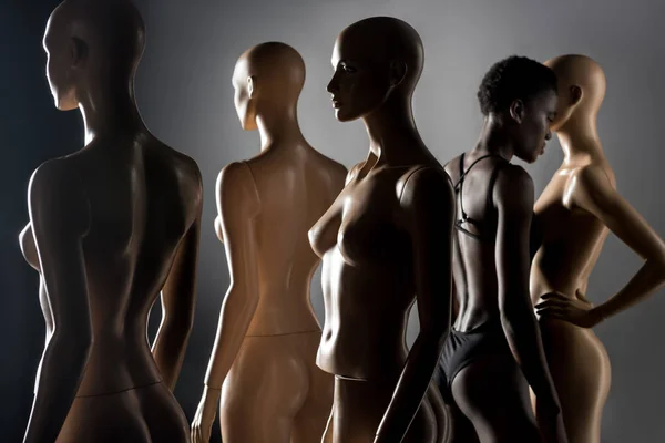 Young african american woman in bodysuit standing between dummies on black — Stock Photo