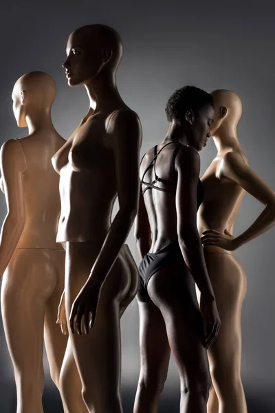 Afroamerikanerin im Body steht zwischen Schaufensterpuppen auf schwarz — Stockfoto