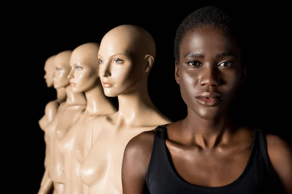 Серьезная африканская американская девушка смотрит в камеру, стоя с манекенами на черном — стоковое фото