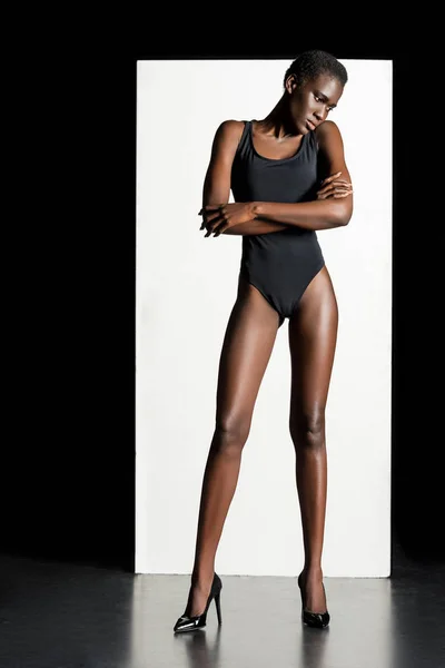 Visão de comprimento total da bela menina americana africana em bodysuit e sapatos de salto alto posando em estúdio — Fotografia de Stock