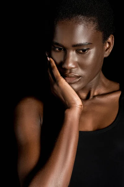 Pensivo jovem afro-americano mulher tocando rosto com a mão e olhando para baixo isolado no preto — Fotografia de Stock