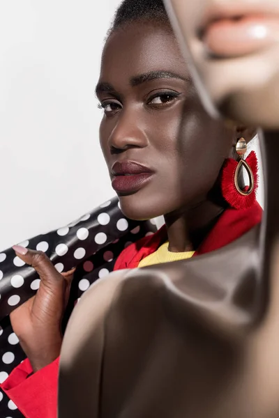 Enfoque selectivo de hermosa mujer afroamericana con bolsa de compras mirando a la cámara en blanco - foto de stock