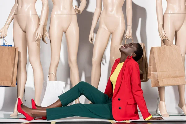 Happy african american woman sitting in front of mannequins with shopping bags — Stock Photo