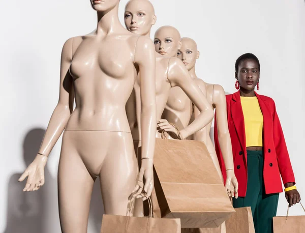 Femme afro-américaine debout en rangée avec des mannequins tenant des sacs en papier sur blanc — Photo de stock