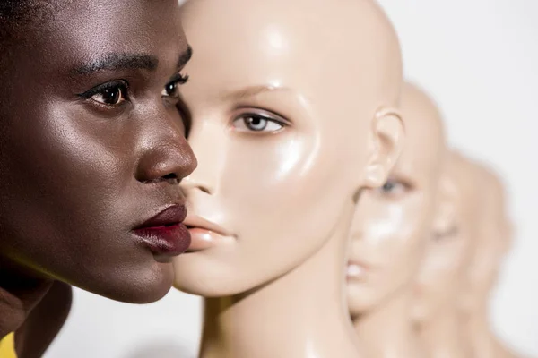 Молодая африканская американка смотрит в сторону, стоя рядом с манекенами на белом — стоковое фото