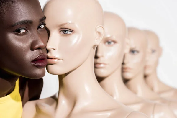 Jeune femme afro-américaine regardant la caméra tout en se tenant près de mannequins sur blanc — Photo de stock
