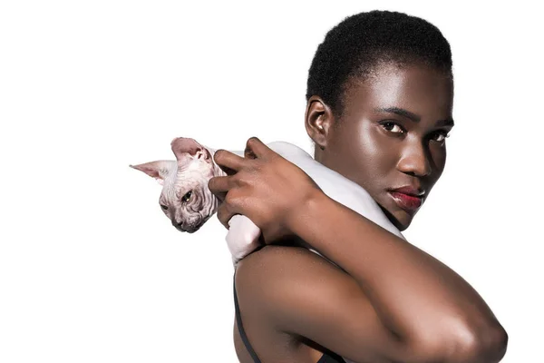 Bela menina americana africana segurando gato esfinge e olhando para a câmera isolada no branco — Fotografia de Stock
