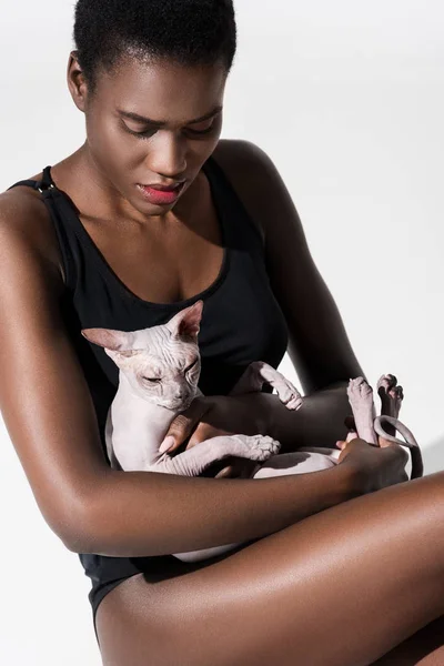Hermosa africana americana mujer en bodysuit holding sphynx gato aislado en blanco - foto de stock
