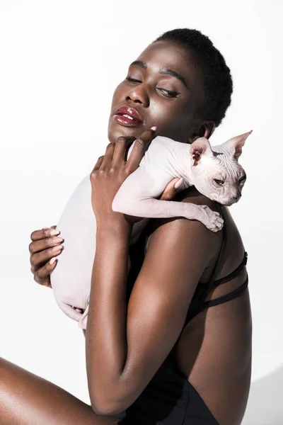 Beautiful sensual african american girl holding sphynx cat isolated on white — Stock Photo