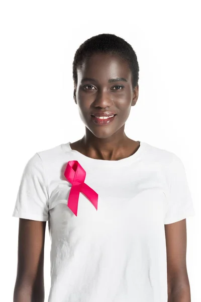 Junge afrikanisch-amerikanische Frau mit rosa Schleife auf T-Shirt lächelt in die Kamera isoliert auf weiß, Brustkrebs-Konzept — Stockfoto