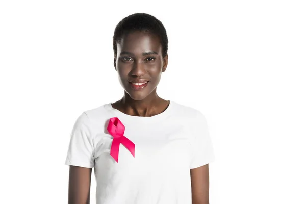 Joven mujer afroamericana con cinta rosa en camiseta sonriendo a cámara aislada en blanco, concepto de cáncer de mama - foto de stock