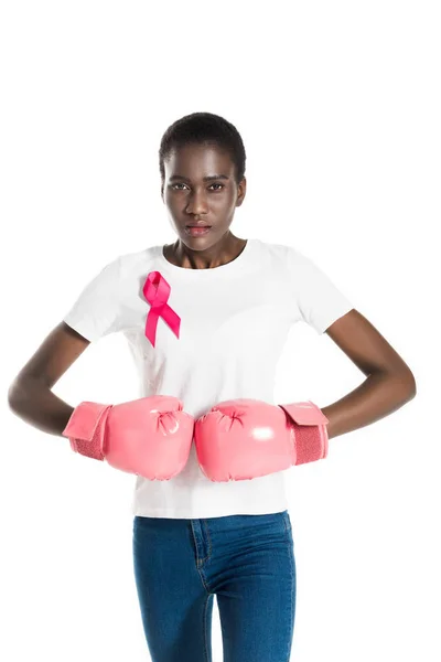 Jeune femme avec ruban rose sur t-shirt portant des gants de boxe et regardant la caméra isolée sur blanc, concept de cancer du sein — Photo de stock