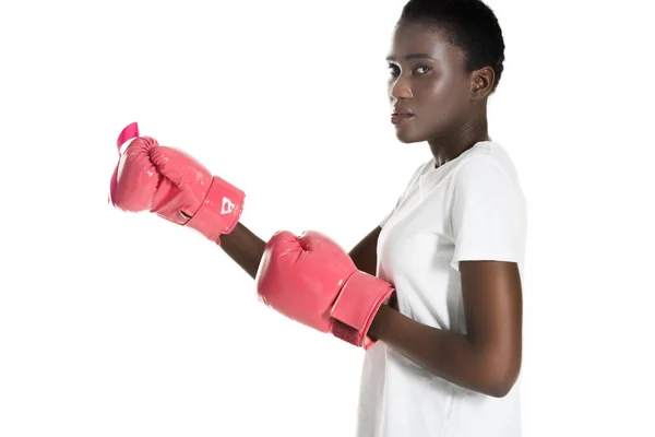 Side view of african american woman in pink boxing gloves looking at camera isolated on white, breast cancer concept — Stock Photo