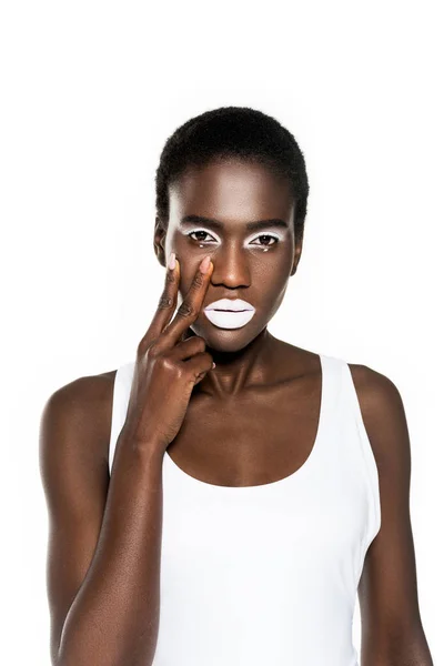 Grave giovane donna africana americana con trucco bianco toccare il viso e guardando la fotocamera isolata su bianco — Foto stock