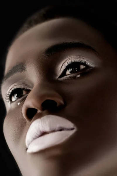 Low angle view of beautiful african american girl with white lips looking away isolated on black — Stock Photo