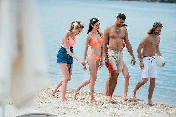 Felices jóvenes amigos con pelota caminando en la playa de arena - foto de stock