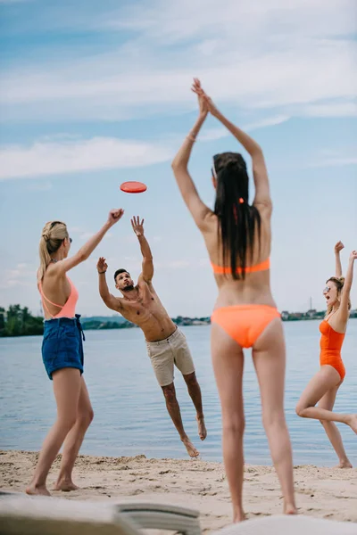 Happy young people playing with flying disc on sandy beach — Stock Photo