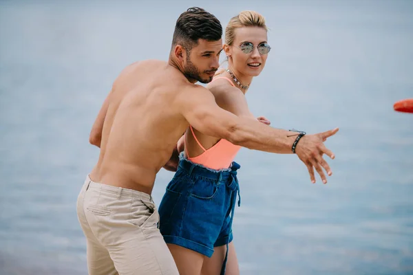 Beautiful happy young couple throwing flying disc on beach — Stock Photo