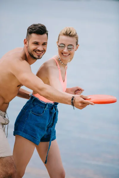 Счастливая молодая пара играет с летающим диском на пляже — стоковое фото