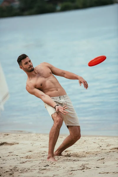 Handsome young man throwing flying disk at sandy beach — Stock Photo