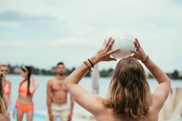 Rückansicht eines jungen Mannes, der mit Freunden am Strand Volleyball spielt — Stockfoto